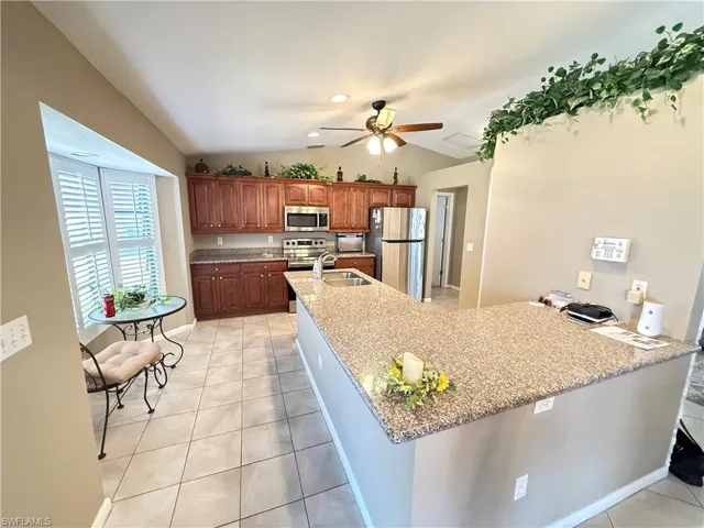 Kitchen with light tile patterned floors, stainless steel appliances, a peninsula, wood finish cabinetry, and a ceiling fan