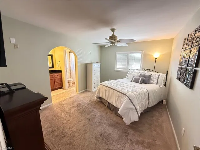 Bedroom featuring arched walkways, light colored carpet, a ceiling fan, and ensuite bath