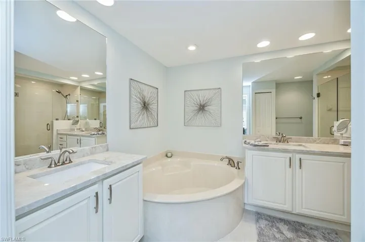 Bathroom featuring a shower stall, two vanities, a bath, and recessed lighting
