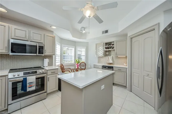 Kitchen with stainless steel appliances, a raised ceiling, a center island, light tile patterned floors, and a ceiling fan