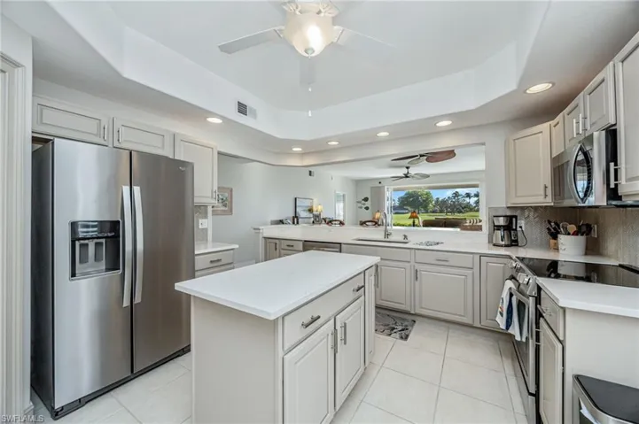 Kitchen with stainless steel appliances, a tray ceiling, recessed lighting, light tile patterned floors, and a center island
