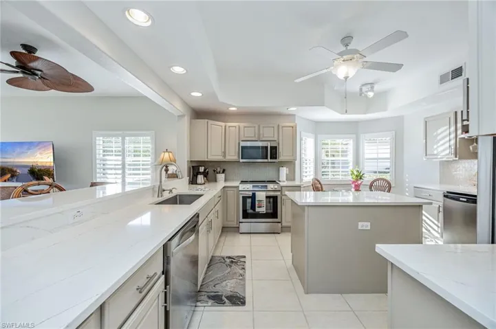 Kitchen with a ceiling fan, a center island, stainless steel appliances, a tray ceiling, and decorative backsplash