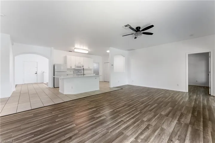 Open-concept living space featuring wood-finish flooring, a white kitchen island with a built-in sink, white cabinetry, and stainless steel appliances