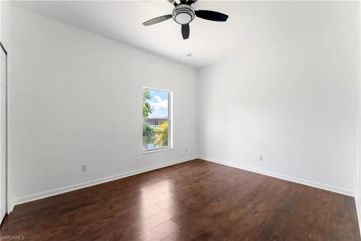 Spacious room featuring rich wood-finish flooring, a contemporary ceiling fan, and a single window overlooking a serene water canal