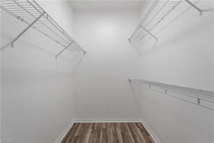 Walk-in closet featuring wire shelving, white painted walls, white baseboards, and wood-finish flooring