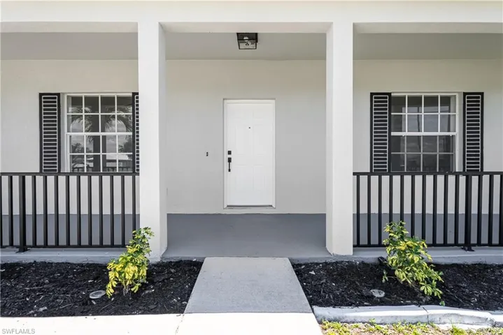 Covered front entrance with a white paneled door, flanked by two multi-pane windows with black louvered shutters