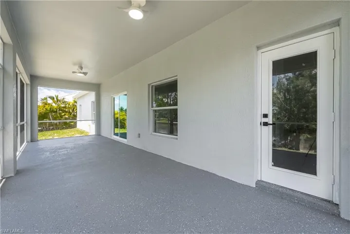 Spacious covered patio featuring a textured floor, white walls, and dual ceiling fans