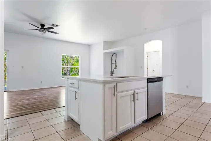 Kitchen island featuring a single-basin sink with a pull-down faucet, white cabinetry, and a built-in stainless steel dishwasher