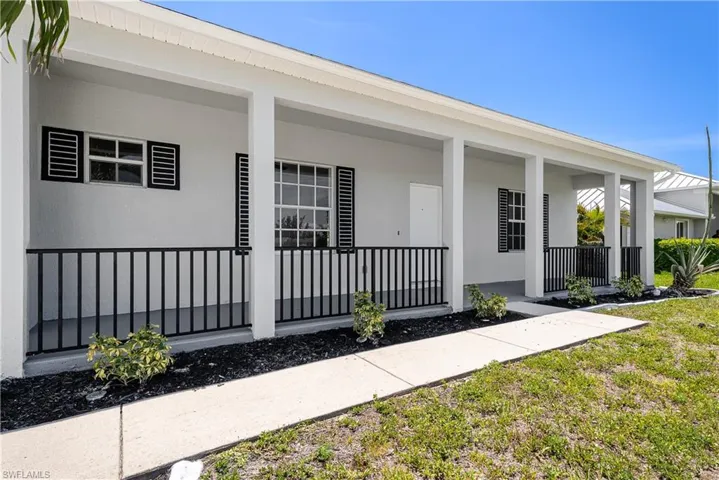 Modern ranch-style home featuring a covered front porch with black iron railings, white exterior walls, multiple windows with black louvered shutters, and a concrete walkway