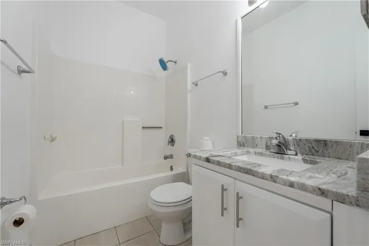 Full bathroom featuring a white tub-shower combination with subway tile surround, a built-in toilet, and a vanity with a light gray veined countertop, an undermount sink, and white cabinetry