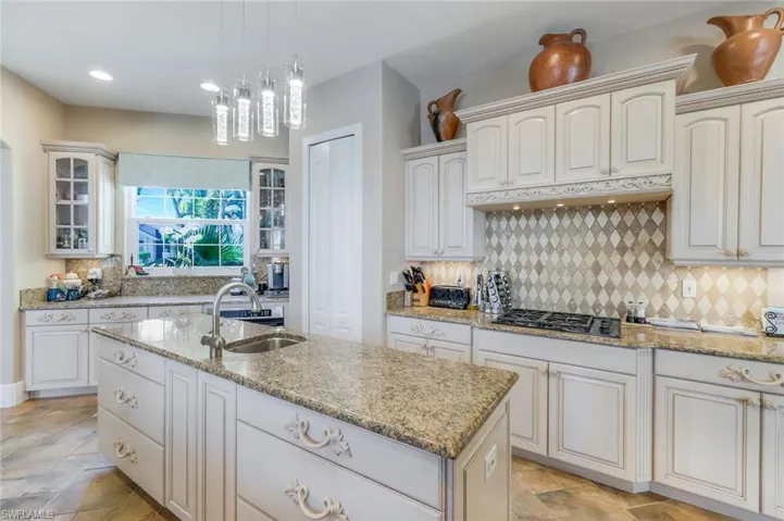 Kitchen with light tile flooring, a center island with sink, tasteful backsplash, stainless steel gas stovetop, and sink