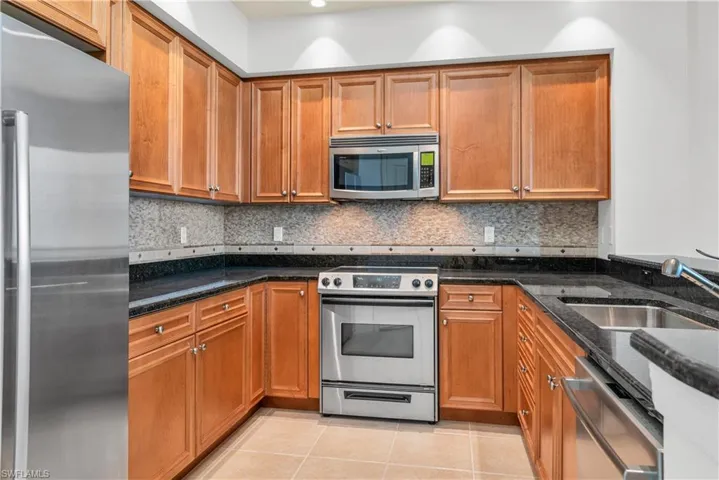 Kitchen featuring dark stone counters, tasteful backsplash, light tile floors, sink, and appliances with stainless steel finishes