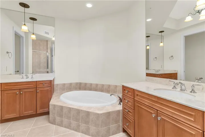 Bathroom with dual sinks, tile flooring, vanity with extensive cabinet space, and tiled tub