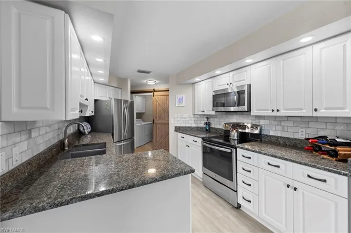 Kitchen featuring white cabinetry, appliances with stainless steel finishes, light wood-style flooring, dark stone counters, and recessed lighting