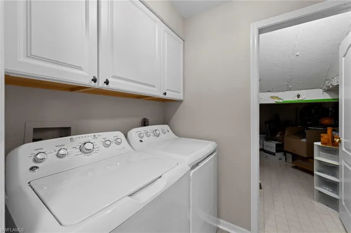 Laundry area featuring cabinet space, washer and clothes dryer, light tile patterned flooring, and a textured wall