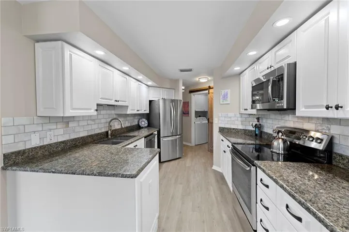 Kitchen with appliances with stainless steel finishes, white cabinets, light wood-style floors, dark stone countertops, and recessed lighting