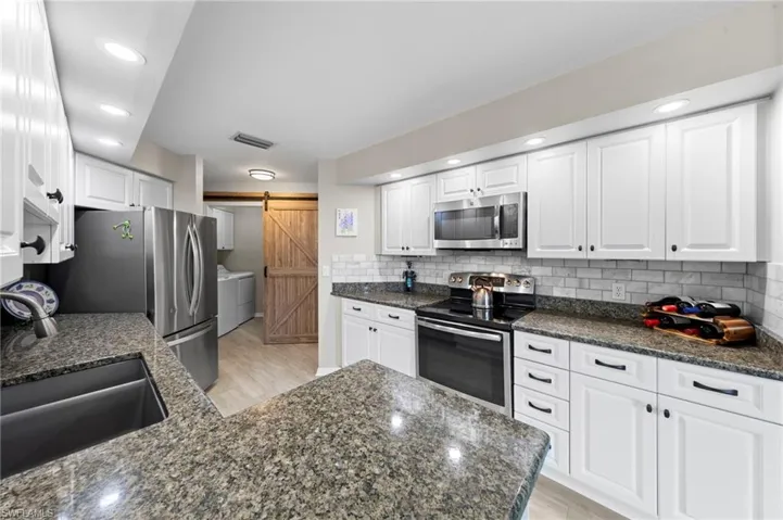 Kitchen featuring appliances with stainless steel finishes, white cabinets, recessed lighting, a barn door, and dark stone counters