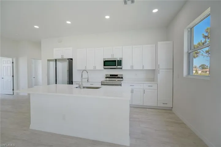 Kitchen with white cabinets, stainless steel appliances, light hardwood / wood-style floors, sink, and a center island with sink