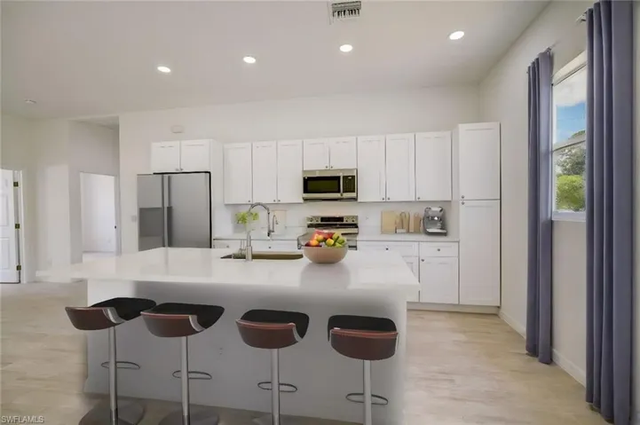Kitchen with stainless steel appliances, white cabinets, sink, light hardwood / wood-style floors, and a kitchen island with sink