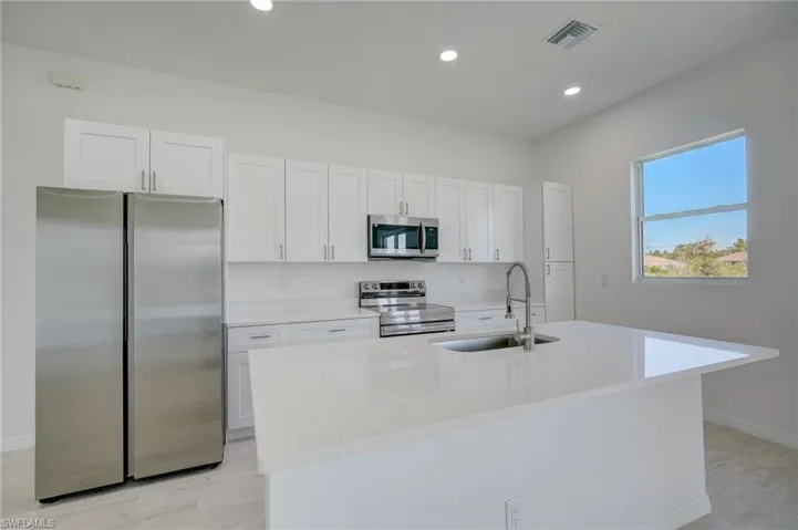 Kitchen with light hardwood / wood-style flooring, an island with sink, stainless steel appliances, and white cabinets