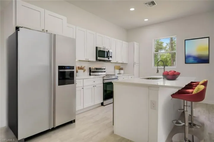 Kitchen with sink, a kitchen breakfast bar, white cabinetry, electric range, and white fridge with ice dispenser