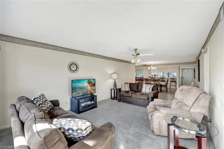 Tiled living area with a ceiling fan, ornamental molding, and a chandelier