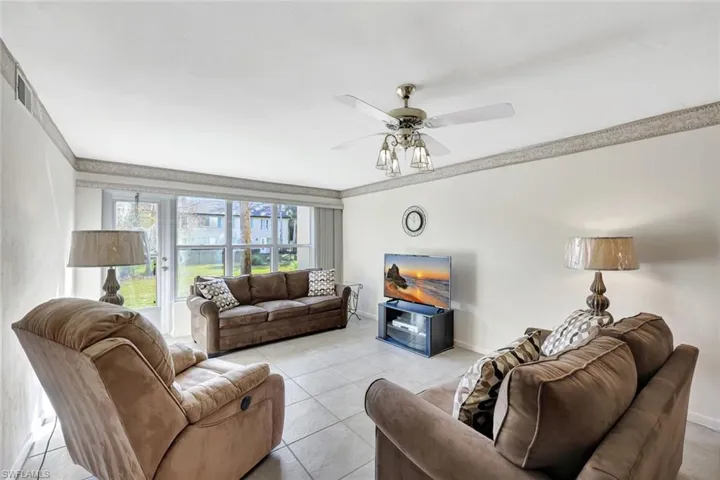 Living room with tile patterned floors, ceiling fan, and crown molding