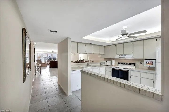 Kitchen with white appliances, a peninsula, ceiling fan, and light tile patterned floors