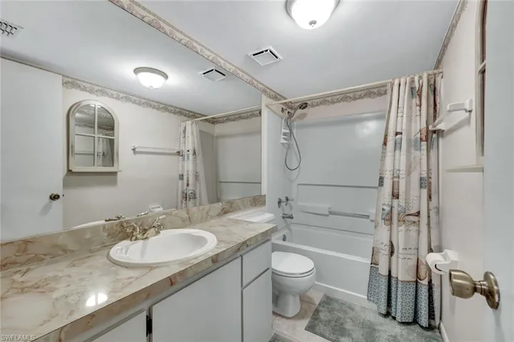 Bathroom with vanity, shower / bathtub combination with curtain, and light tile patterned floors