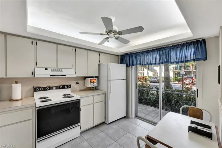 Kitchen featuring white appliances, a raised ceiling, light countertops, and under cabinet range hood