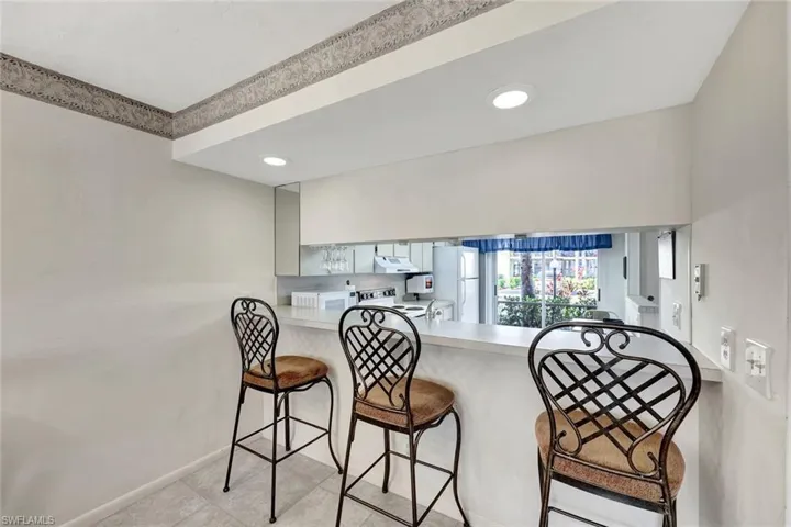 Kitchen featuring a breakfast bar area, light countertops, white appliances, under cabinet range hood, and recessed lighting