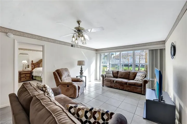 Living area with ceiling fan, light tile patterned floors, and crown molding