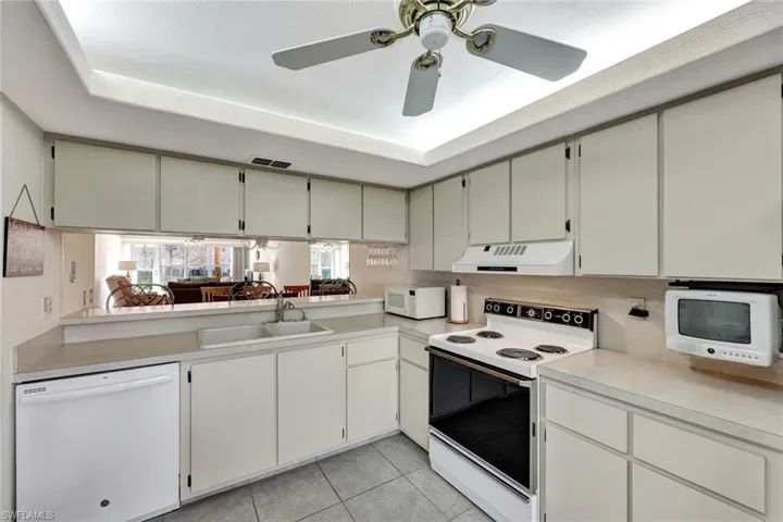 Kitchen with white appliances, light countertops, under cabinet range hood, white cabinets, and light tile patterned floors