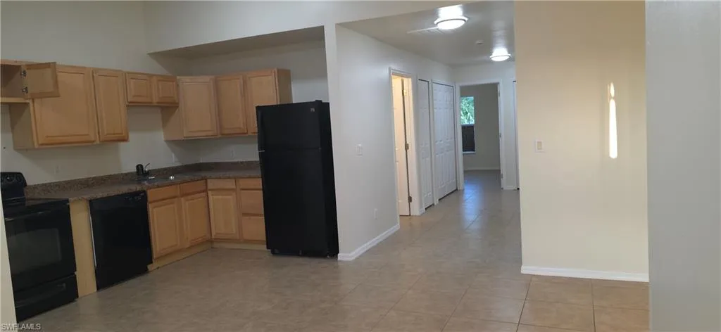 Kitchen with black appliances, light brown cabinetry, and light tile patterned floors