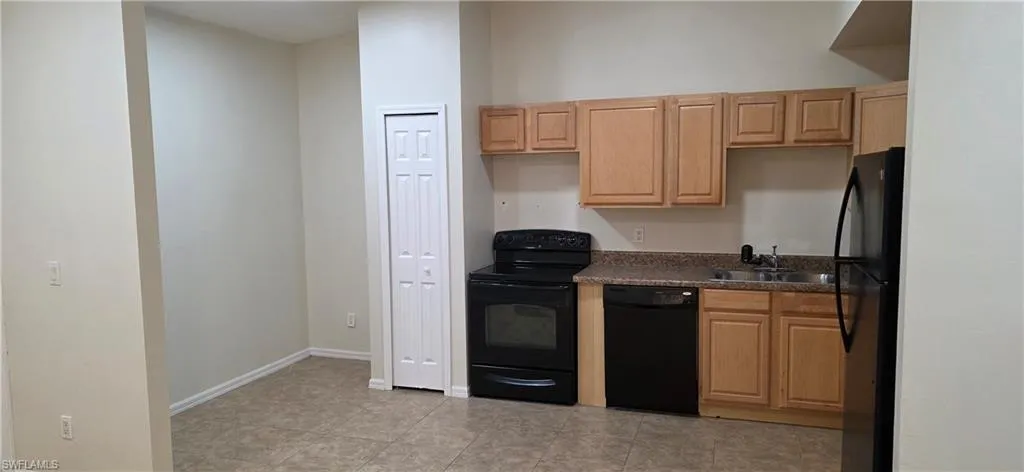 Kitchen featuring black appliances, dark countertops, light brown cabinets, and light tile patterned floors