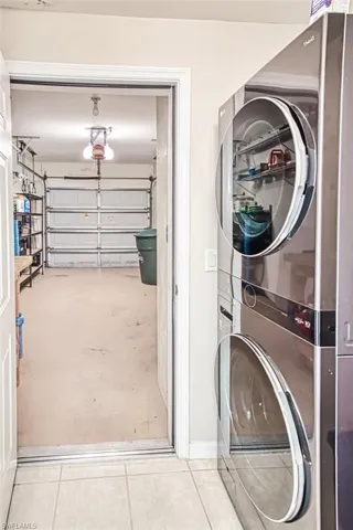 Laundry room featuring stacked washer and clothes dryer, a garage, and tile patterned floors