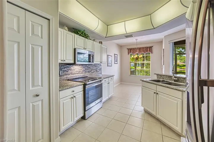 Kitchen featuring stainless steel appliances, a sink, light tile patterned flooring, tasteful backsplash, and baseboards