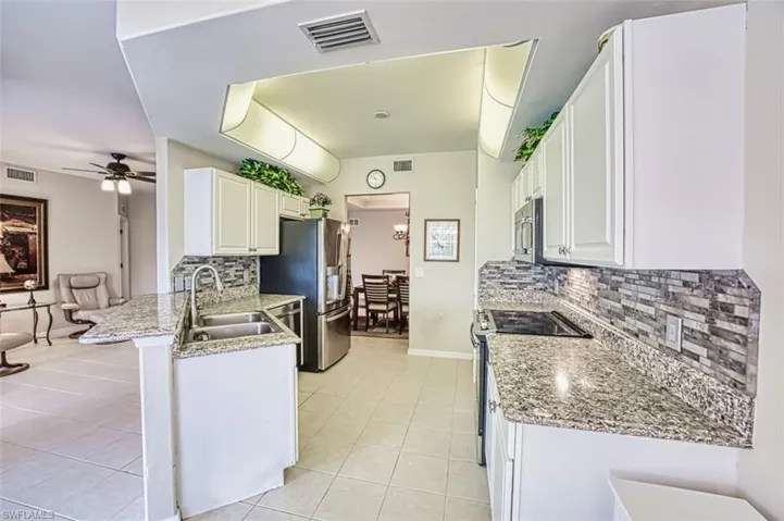 Kitchen with a sink, appliances with stainless steel finishes, light tile patterned floors, backsplash, and a peninsula