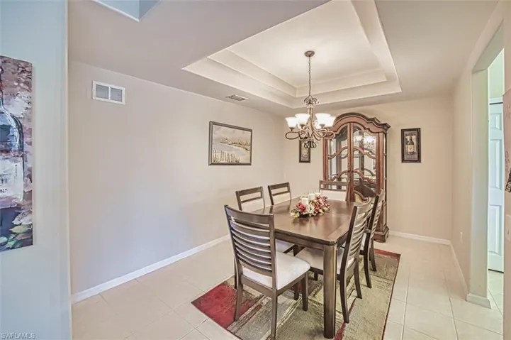 Dining room with a tray ceiling, light tile patterned floors, a chandelier, and baseboards