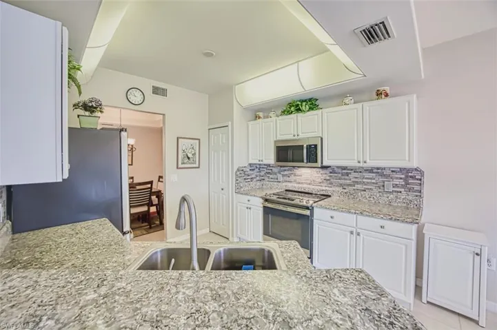 Kitchen featuring stainless steel appliances, a sink, decorative backsplash, and white cabinetry