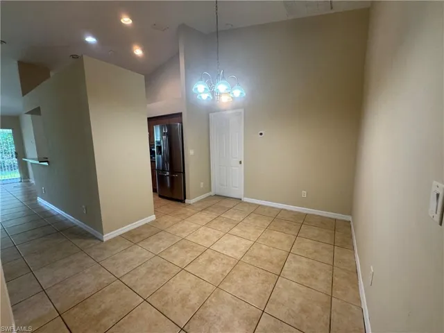 Empty room with a chandelier, light tile patterned flooring, high vaulted ceiling, and recessed lighting