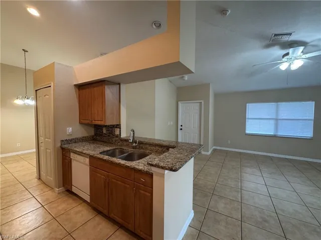 Kitchen featuring light tile patterned floors, a ceiling fan, dark stone counters, dishwasher, and a peninsula