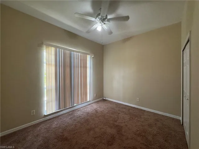 Carpeted spare room with ceiling fan and baseboards
