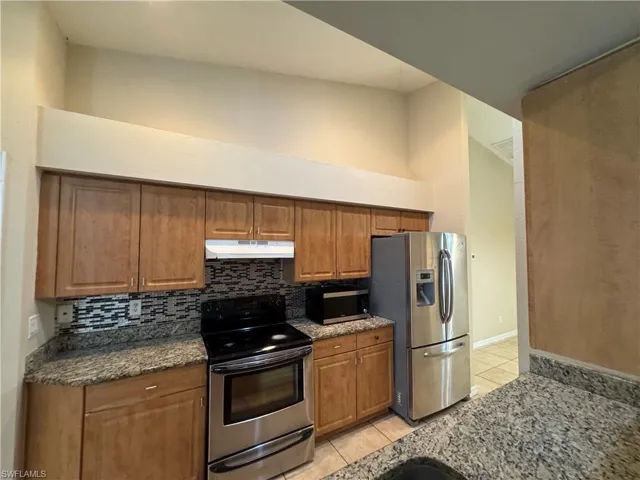 Kitchen with stainless steel appliances, light tile patterned flooring, decorative backsplash, and brown cabinetry