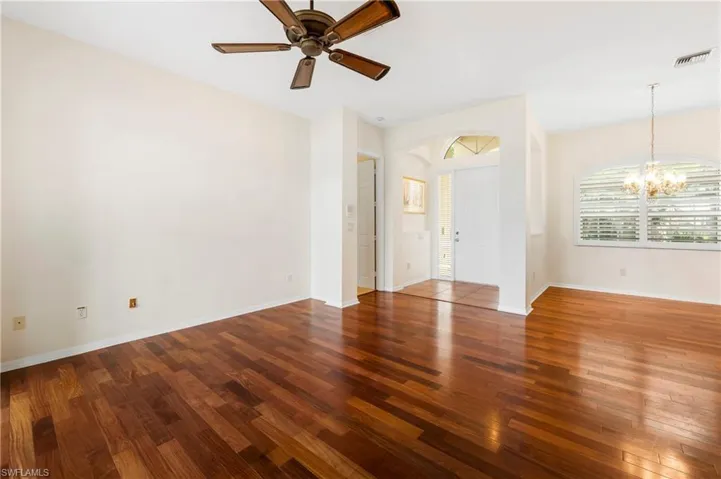 Wood-finish flooring throughout, featuring a ceiling fan, arched doorways, a front entry with a transom window, and an arched window with plantation shutters