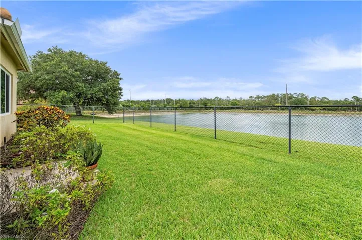 Expansive lawn area featuring a black chain-link fence, mature trees, and a tranquil water feature