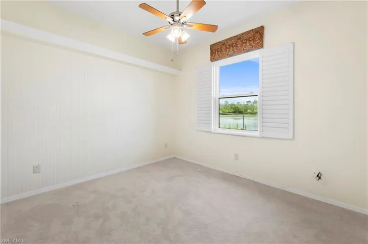 Carpeted room with a ceiling fan, a window featuring white plantation shutters, and an outdoor water feature