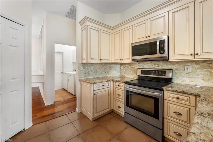 Kitchen featuring cream-colored cabinetry with decorative molding, stainless steel appliances, and stone countertops