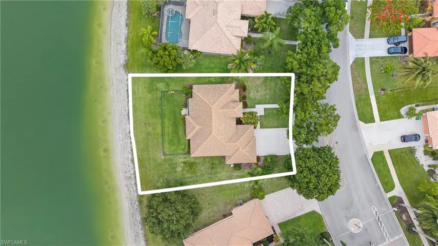 Waterfront property featuring a tile roof, mature landscaping, and a paved driveway