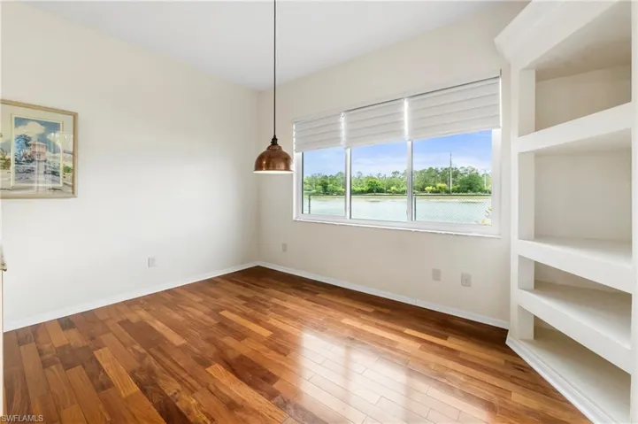 Wood-finish flooring throughout, featuring a window with water and tree scenery, a built-in shelving unit, and a pendant light fixture